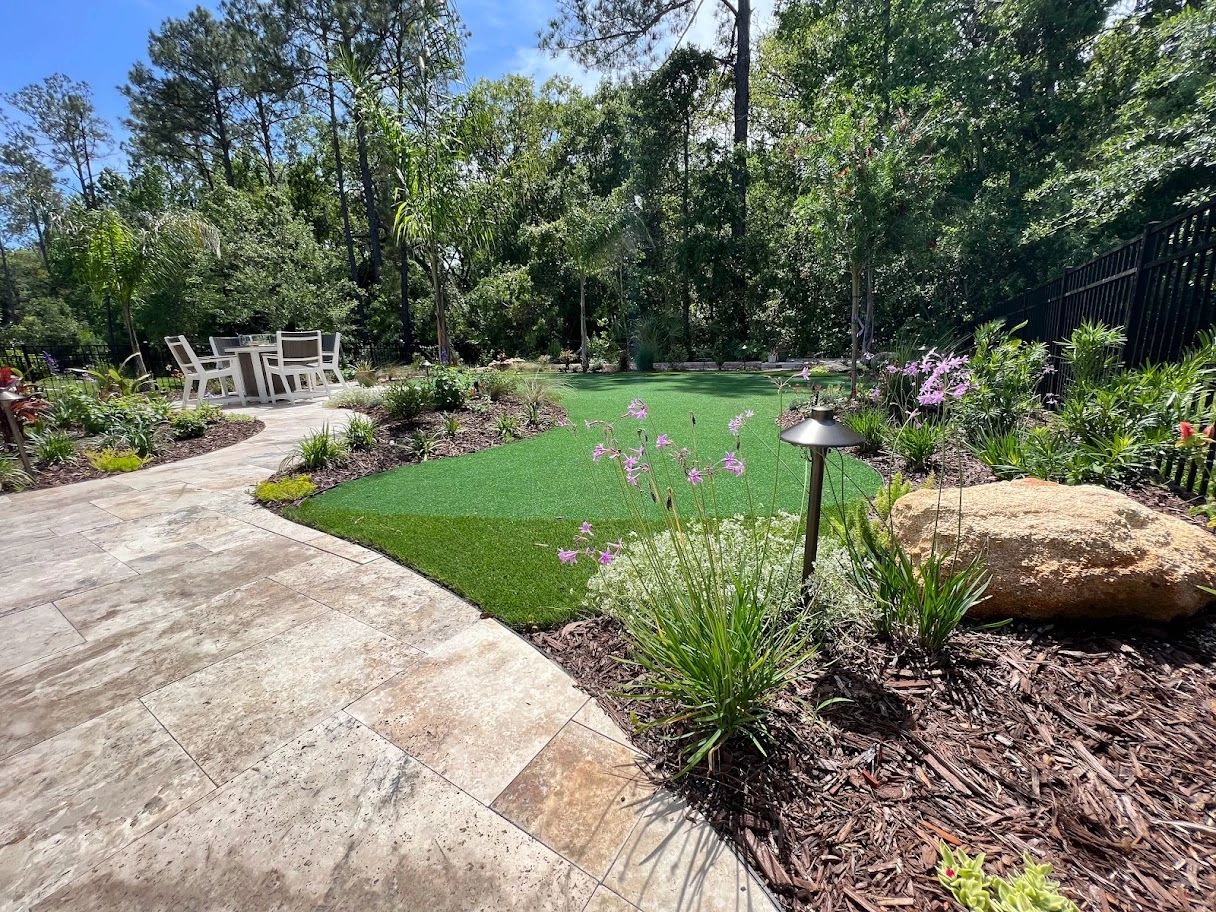 Backyard with a paved patio, putting green, landscaped garden, and outdoor dining set.