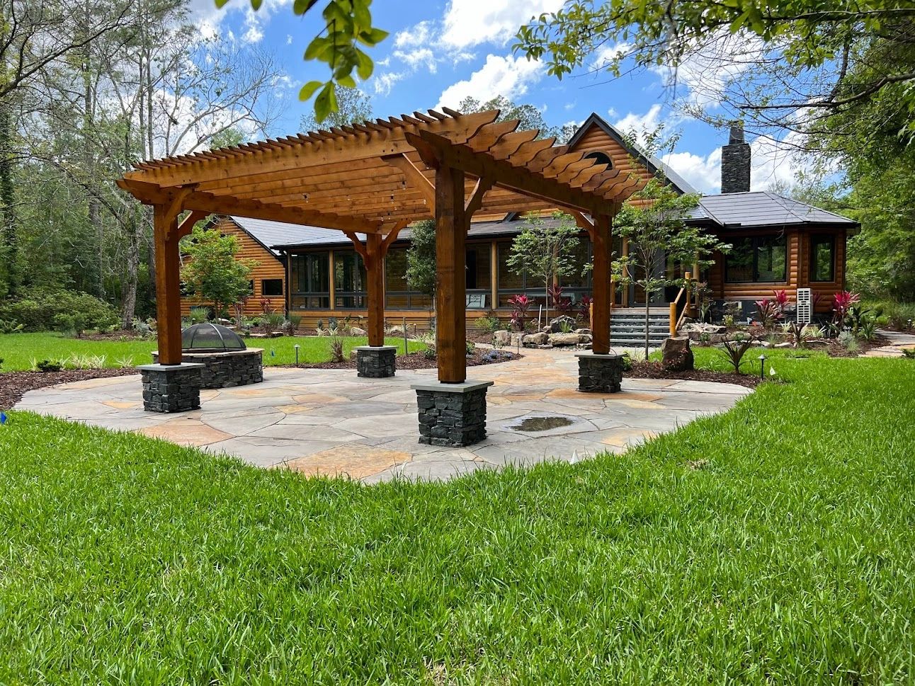 Backyard with wooden pergola, stone fire pit, flagstone patio, and cozy log cabin in the background.