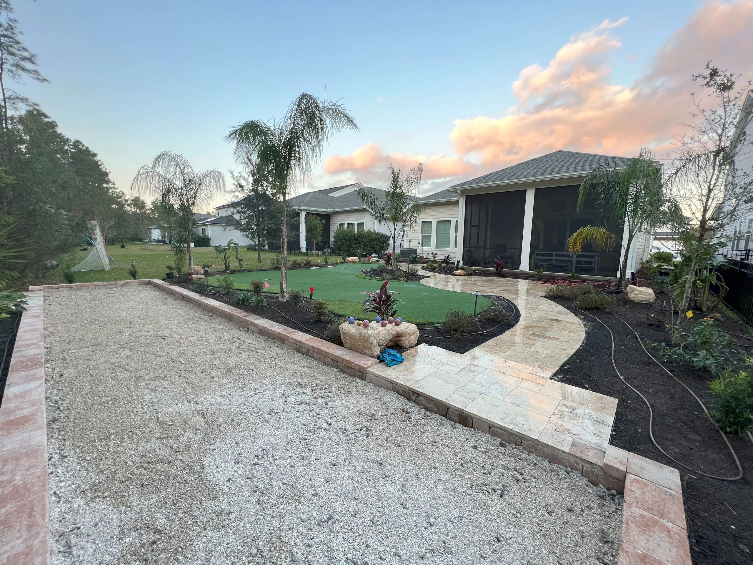 Backyard with a bocce court, putting green, landscaped garden, palm trees, and a screened patio.