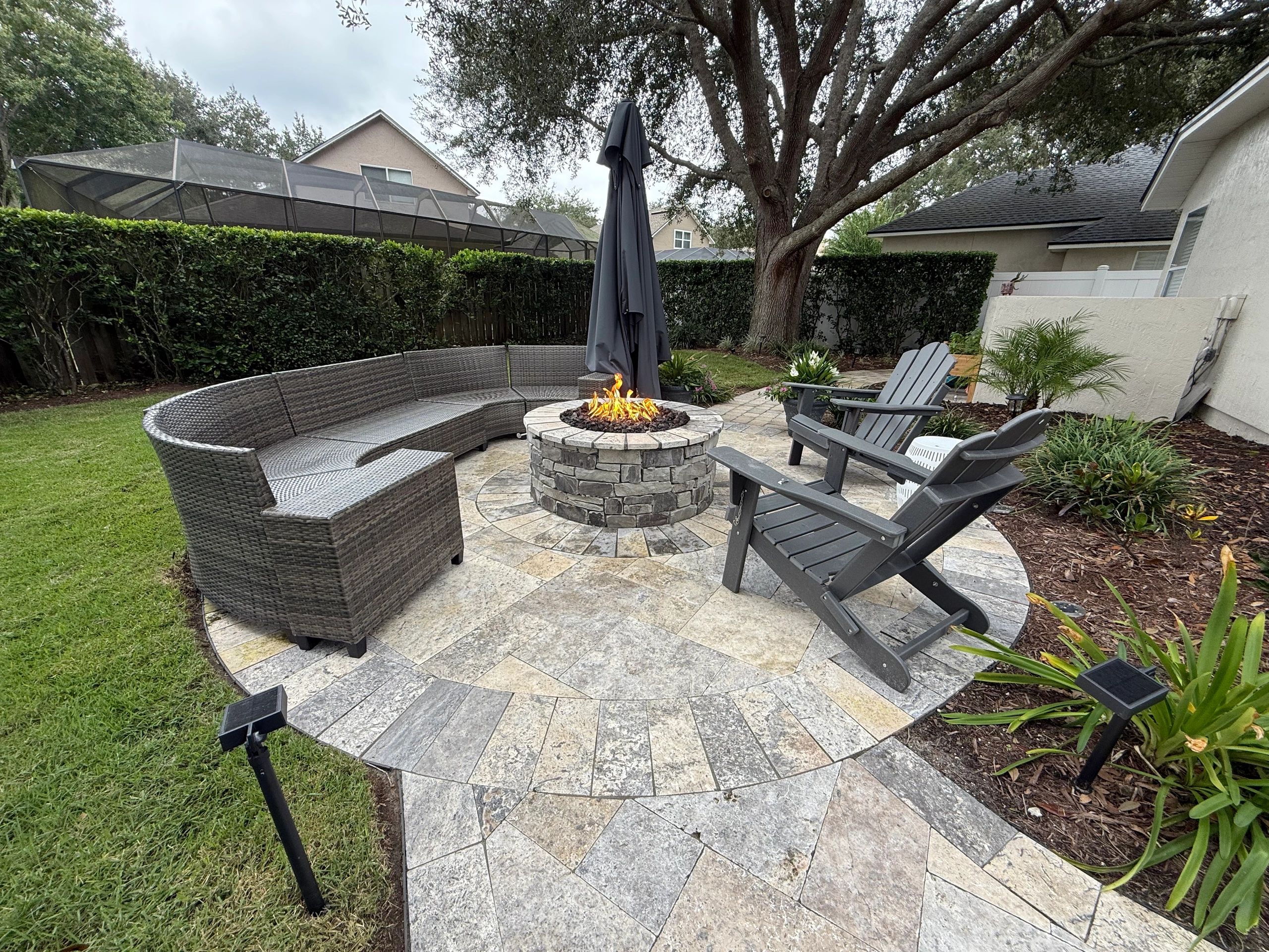 Circle Travertine patio with stone fire pit. Chairs and sectional surrounding a lit fire.