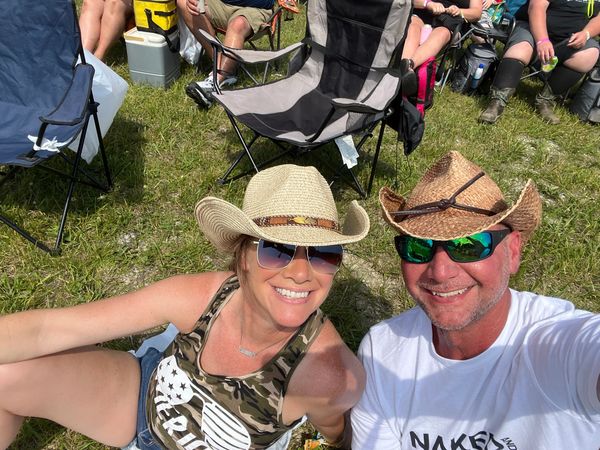 A smiling couple in cowboy hats enjoying an outdoor event on the grass.