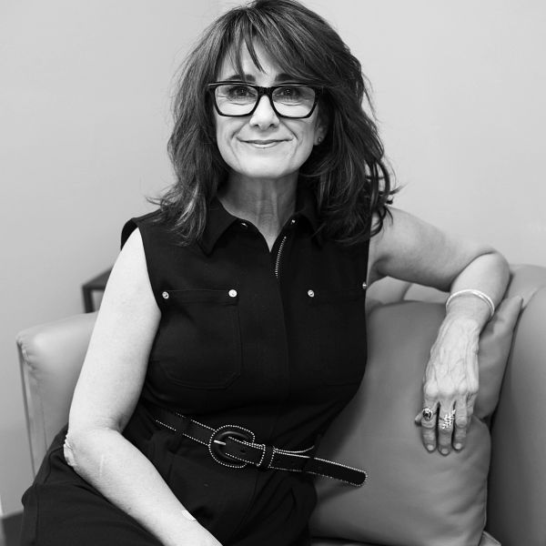 Smiling woman with glasses sitting on a couch.