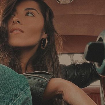 A woman sitting in a classic car smiling while looking out the window 