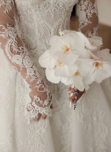Bride holding a white orchid bouquet in a lace wedding dress.