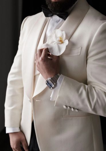 Man dressed in a white tuxedo with a black bow tie and buttonhole florals.