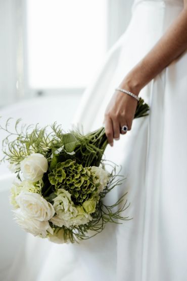 Bride holding a bouquet of white and green flowers.