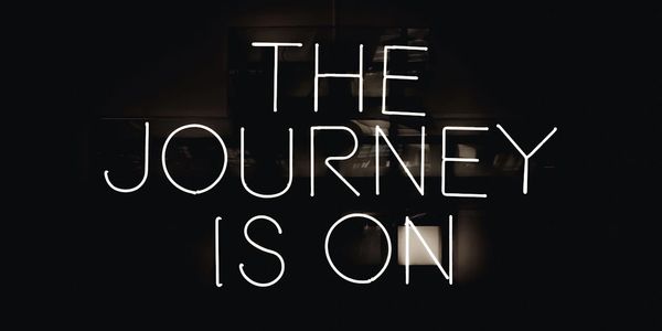 Neon sign displaying 'THE JOURNEY IS ON' in a dark setting.