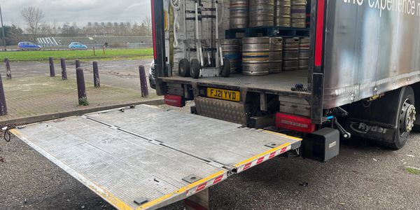 Picture of back of lorry storing beer barrels, with tail lift lowered at the back. 