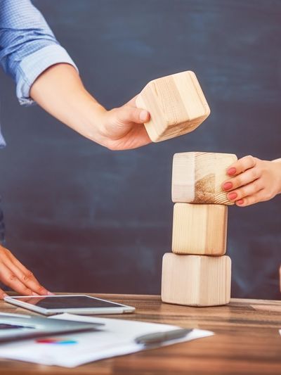 Two people stacking wooden blocks on a desk with papers and a tablet.
