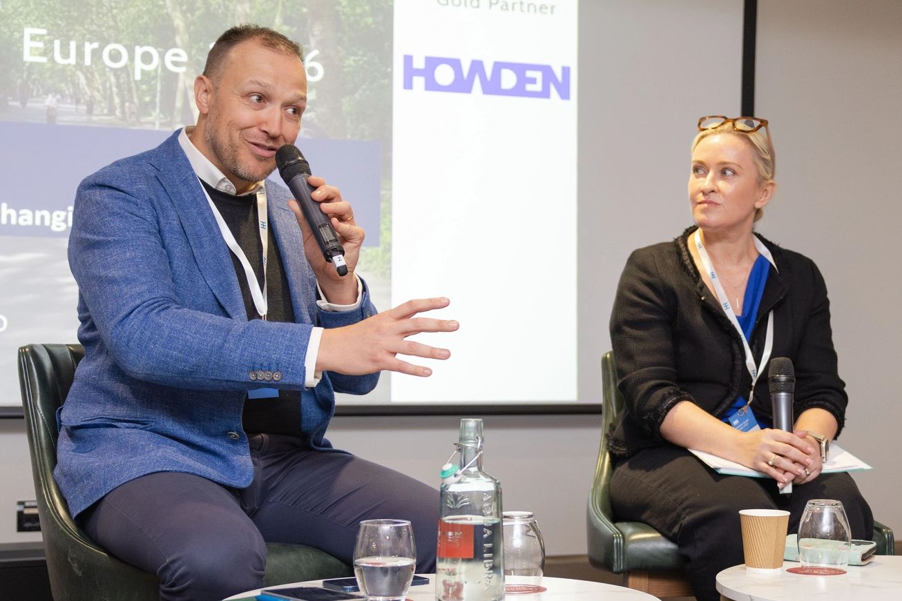 Man speaking into a microphone while woman listens during a panel discussion.