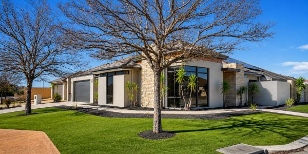 Modern house with a well-maintained lawn and leafless trees under a clear blue sky.