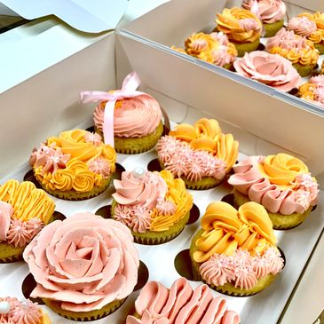Box of beautifully decorated pink and yellow floral cupcakes.