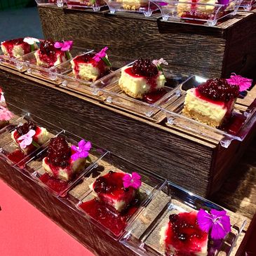 Mini cheesecakes with berry topping and edible flowers on clear plates.