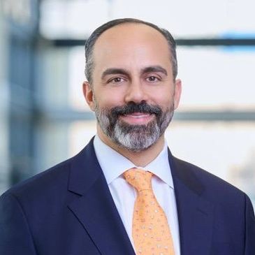 Professional man with a beard in a suit and orange tie smiling.