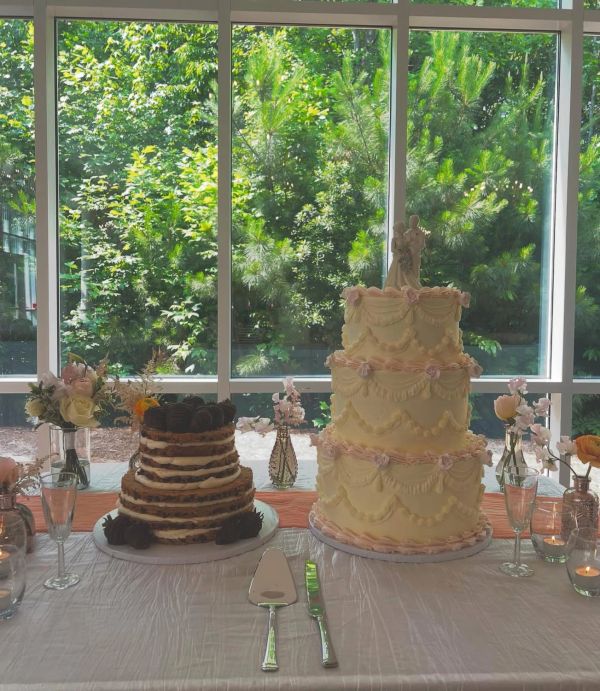 Two decorated cakes on a table with flowers and greenery background.
