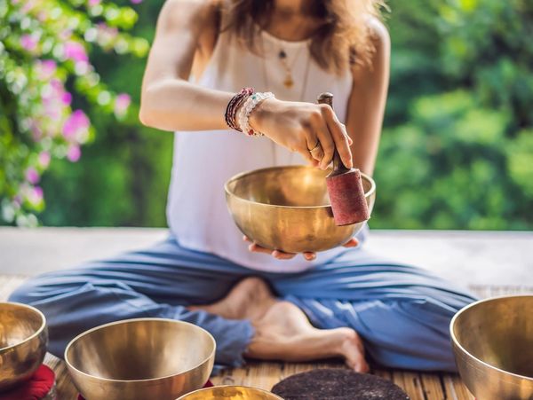 A woman holds a gold Tibetan singing bowl in her hand and uses a mallet to make it sing.