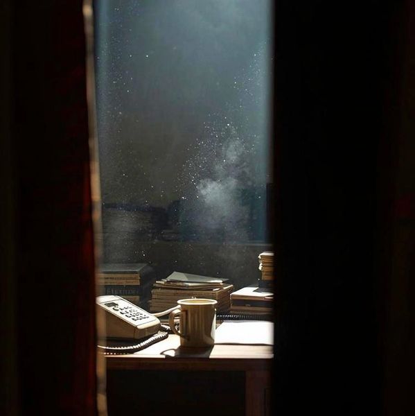 Sunlit desk with a mug, telephone, and stacked books, seen through a narrow gap.