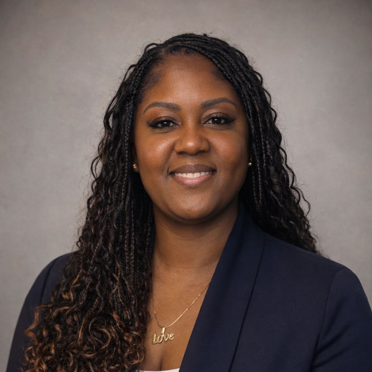 Professional woman with braided hair smiling warmly in a navy blazer.