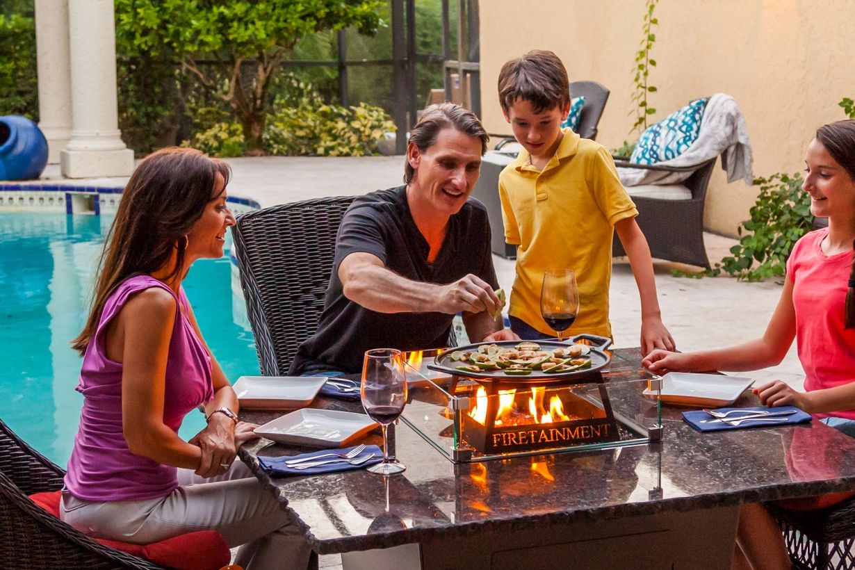 Family of four enjoying a hibachi-style meal in the center of their square gas fire pit Madrid table