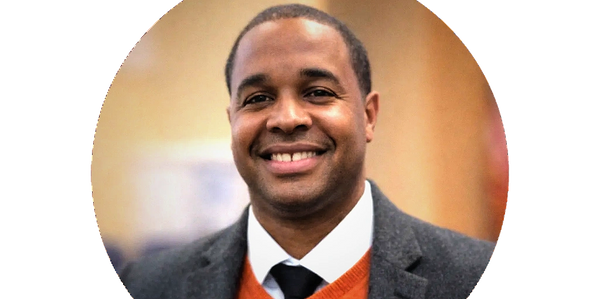 Smiling man in a gray blazer and orange sweater.