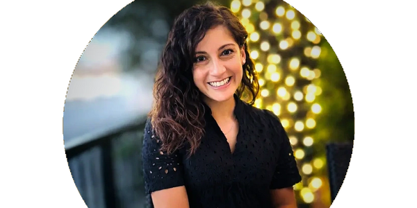 Smiling woman with curly hair sitting at a table with lights in the background.