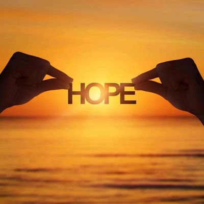 Hands holding the word 'HOPE' against a golden sunset over the ocean.