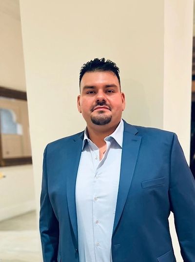 Man dressed in a blue suit and white shirt standing indoors.