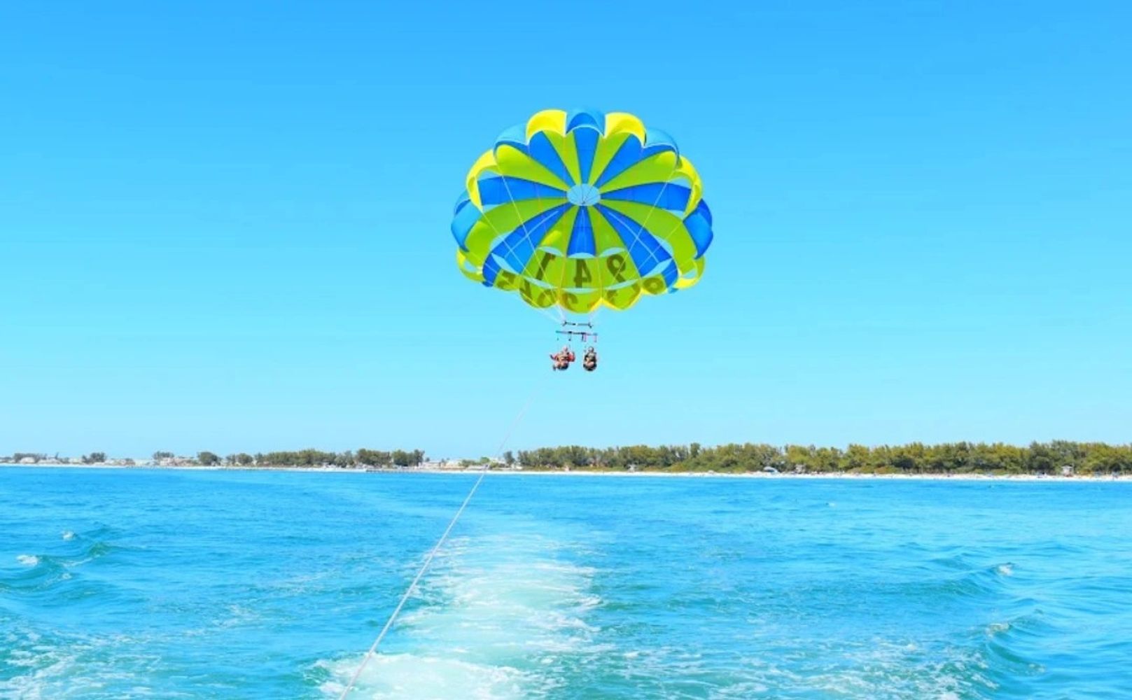 Two people parasailing over clear blue ocean water on a sunny day.