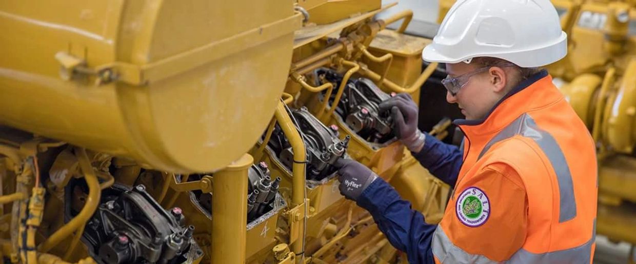 Louise working on a large Caterpillar engine wearing a hard hat and hivis shirt