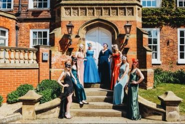 A group of women dressed in elegant evening gowns posed on steps outside a brick building.