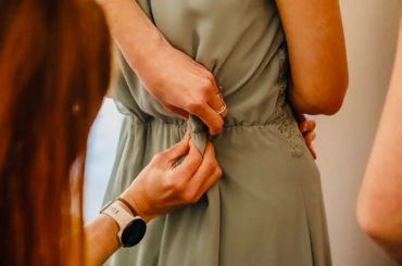 Hands adjusting the back of a green dress on a woman.