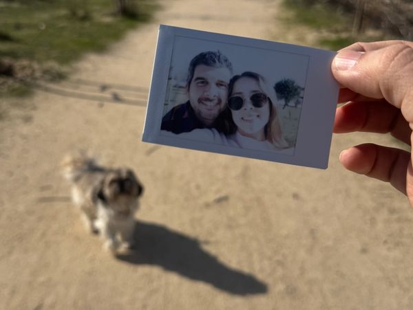 Persona sosteniendo una foto de dos personas con un perro al fondo.