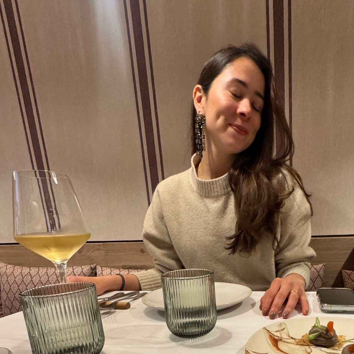 Mujer disfrutando una cena con una copa de vino blanco.