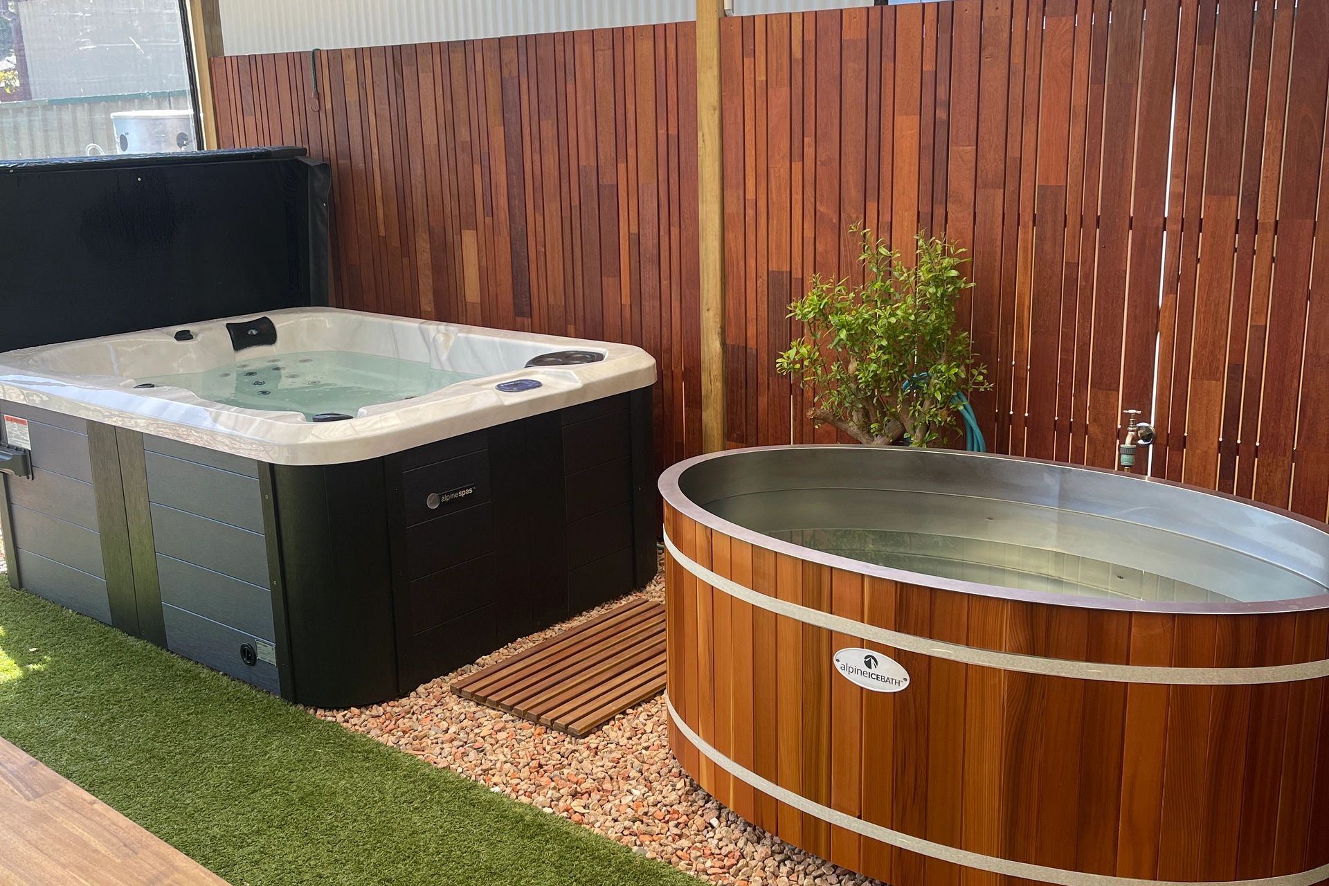 Two outdoor hot tubs next to a wooden fence.