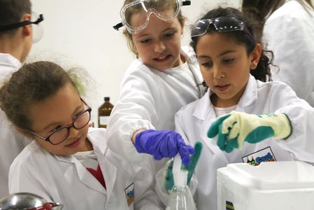 Three kids in lab coats and gloves conducting a science experiment.