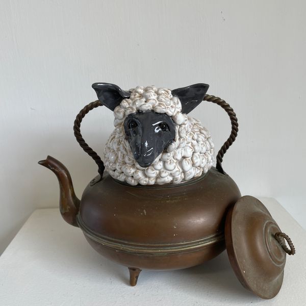 Wooly white sheep with a black face in a copper teapot