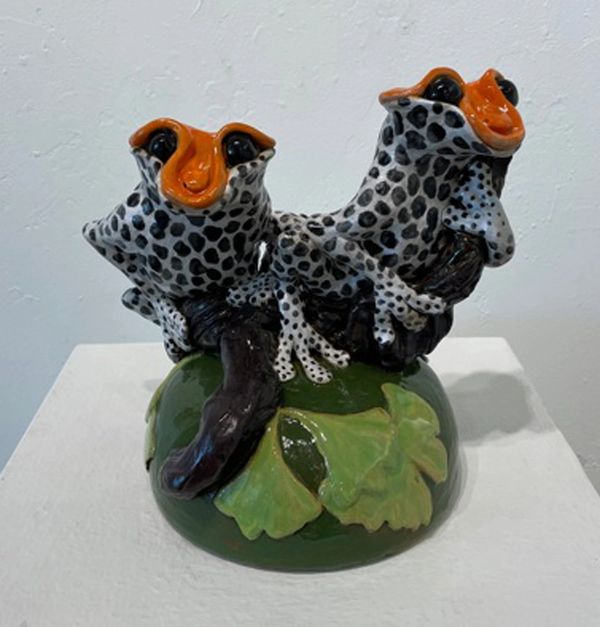 Two black , white and orange frogs on a log on a green mound