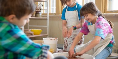 Children happily making pottery on wheels in a bright studio.