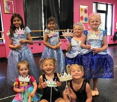 Seven girls in costumes holding crowns and smiling.