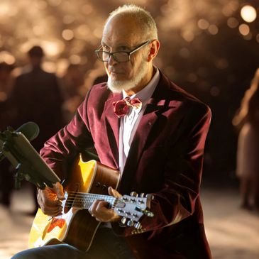 Elderly man playing acoustic guitar with focused expression.