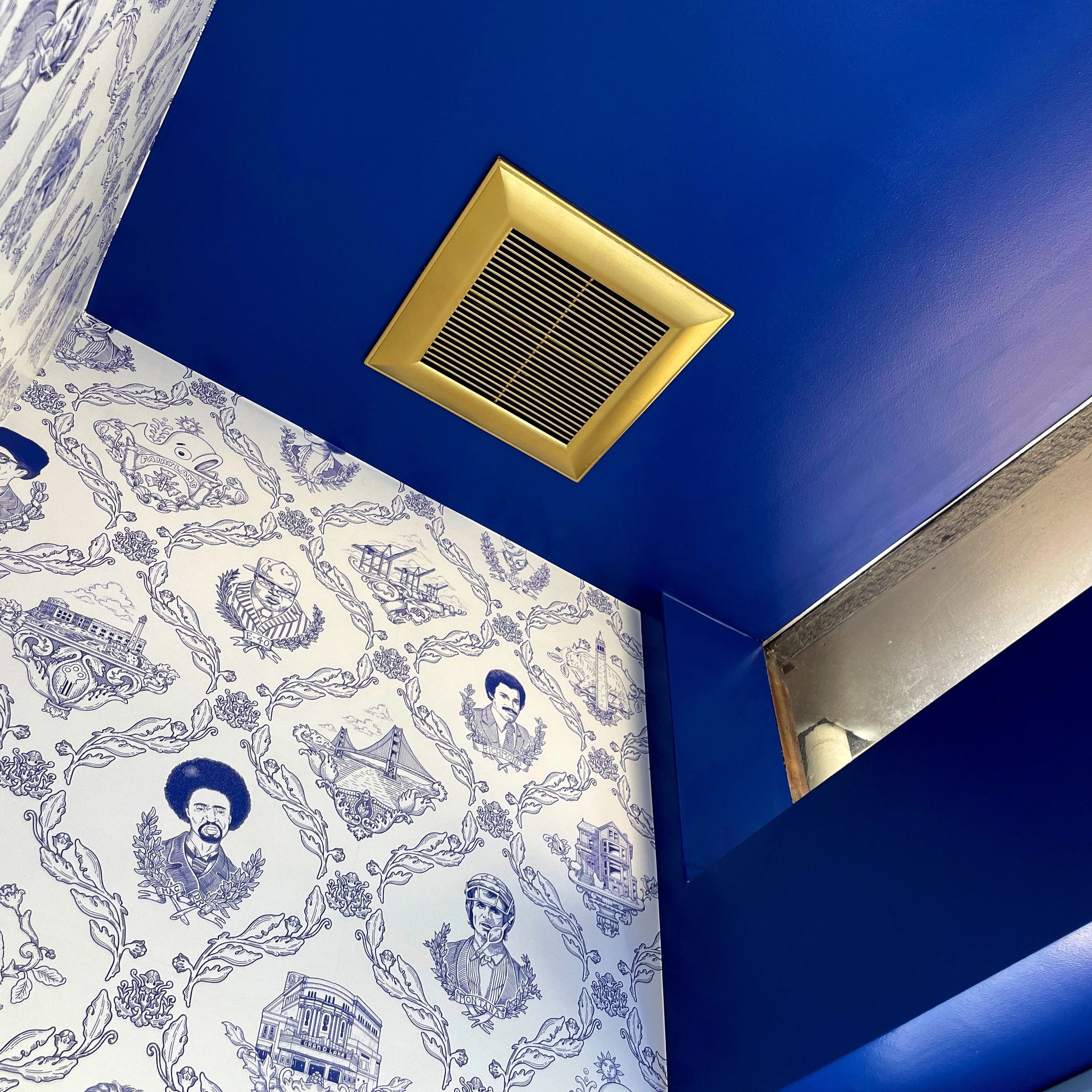 Blue ceiling with a golden vent and illustrated wallpaper on the walls.