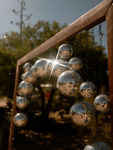 Reflective disco balls hanging on a wooden frame outdoors.