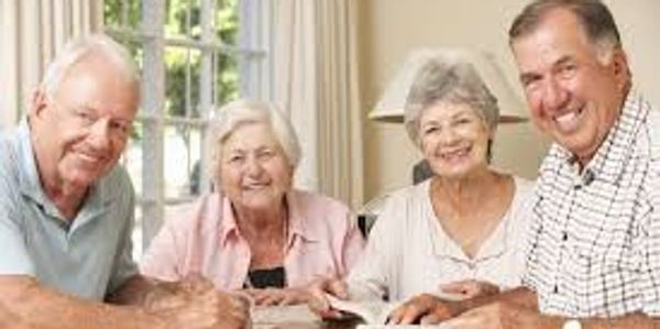 Four elderly friends smiling around a table indoors.