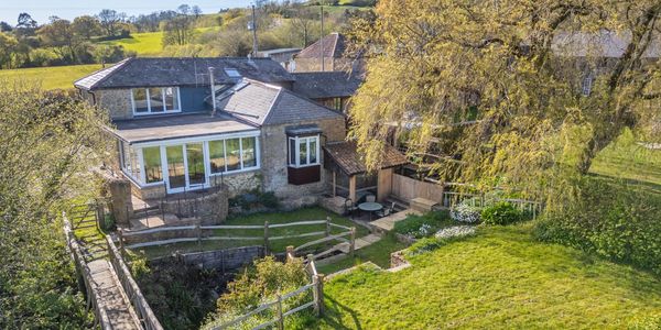 Charming countryside stone house with a wooden bridge and lush garden in spring.