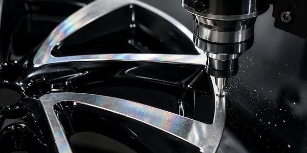 CNC machine shaping a shiny metal car wheel rim.