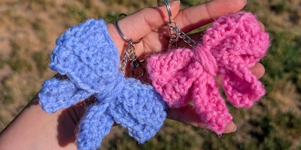 Hand holding two crocheted bow keychains in blue and pink.