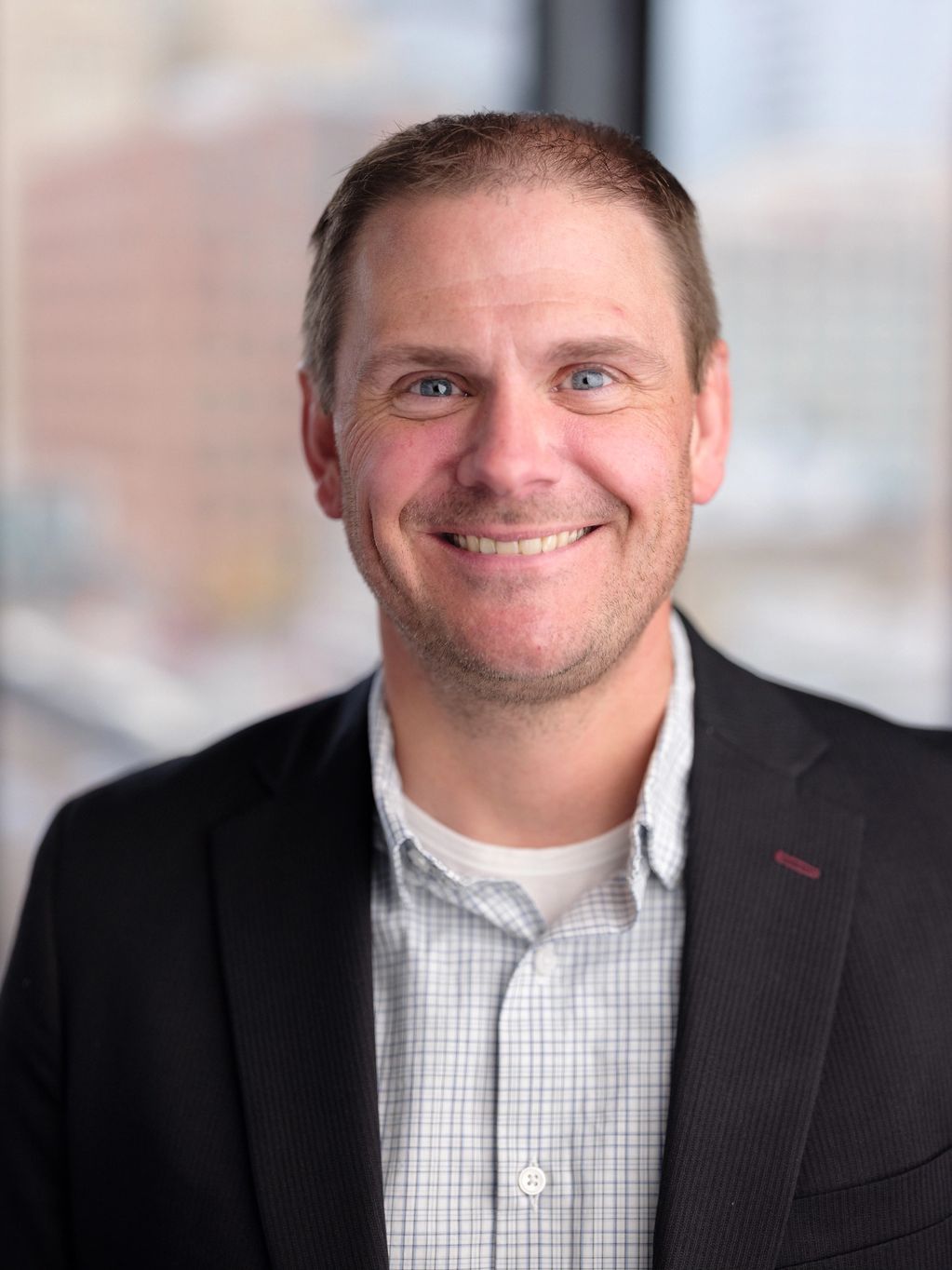 Smiling man in a checkered shirt and black blazer.