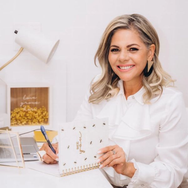 Woman smiling while holding a notebook at a desk.