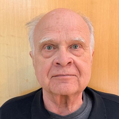 Portrait of an elderly man with light eyes and white hair against a wooden background.
