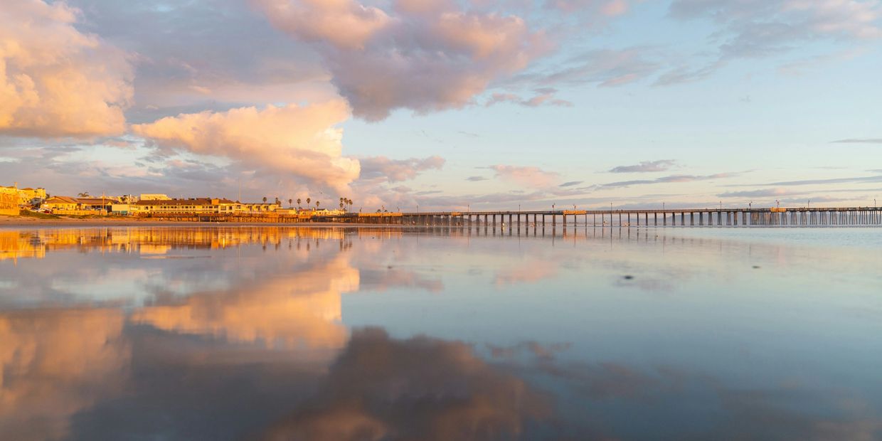 Sunset reflecting on calm water near a coastal pier and buildings.